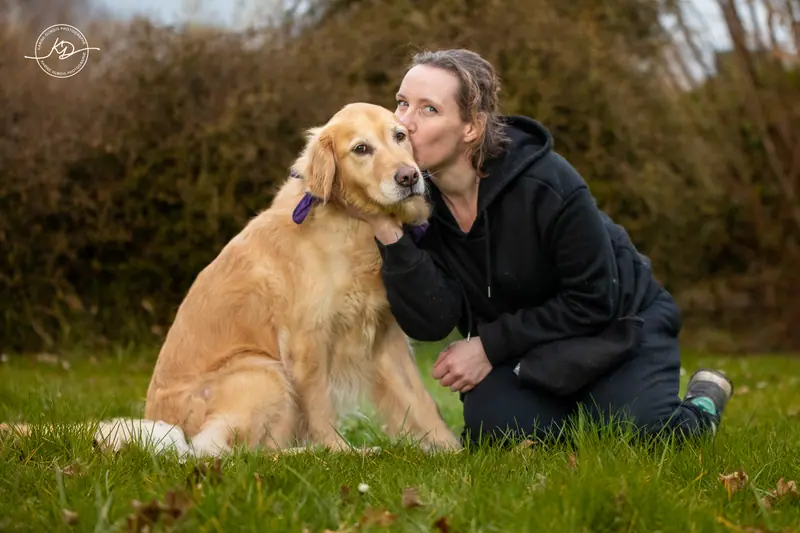 Une femme embrasse un golden retriever assis dans l’herbe, complicité entre humain et chien